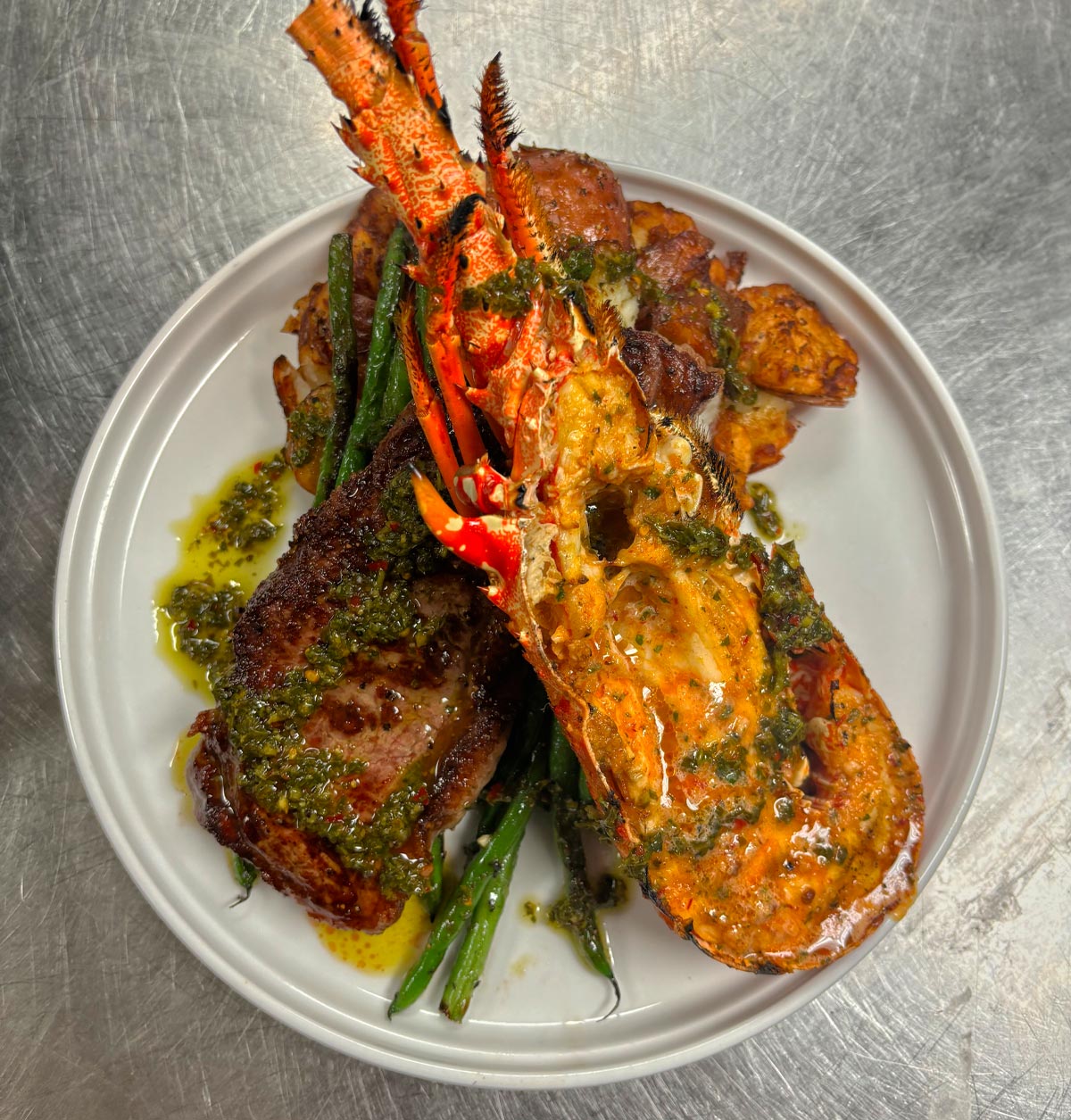 Warm water half spiny lobsters paired with 8-ounce sirloin steaks, served with crispy redskin potatoes and sautéed green beans. Finished with chef's chimichurri and chipotle garlic compound butter.